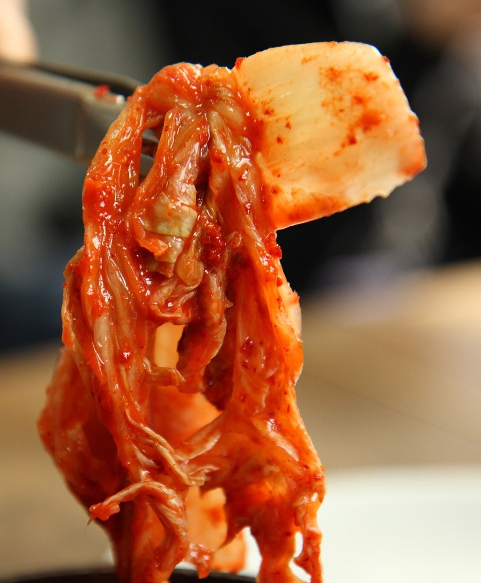 Kimchi being held up by chopsticks, close-up.