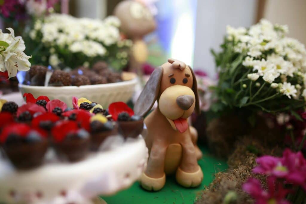 Cute fondant dog amidst colorful desserts and flowers on table.