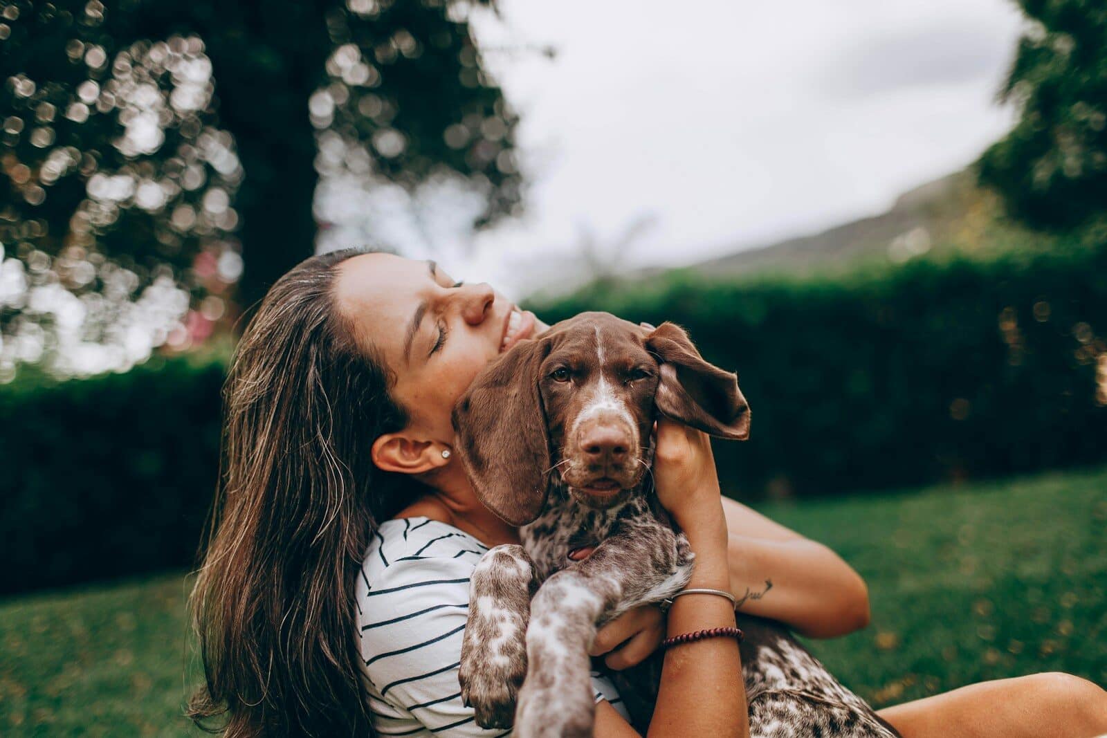 Photo by Helena Lopes woman in white and black stripe tank top hugging brown and white short coated dog